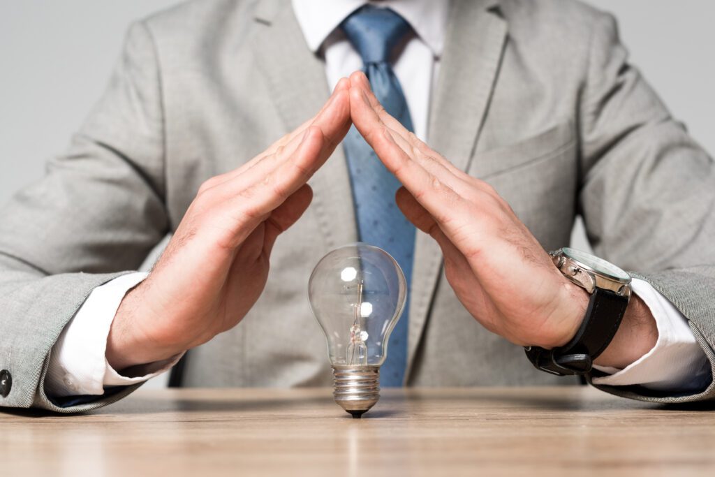 Intellectual Property for Startups: An Essential Guide to Safeguarding Your Business Assets 1 cropped view of businessman showing protection gesture above light bulb isolated on grey